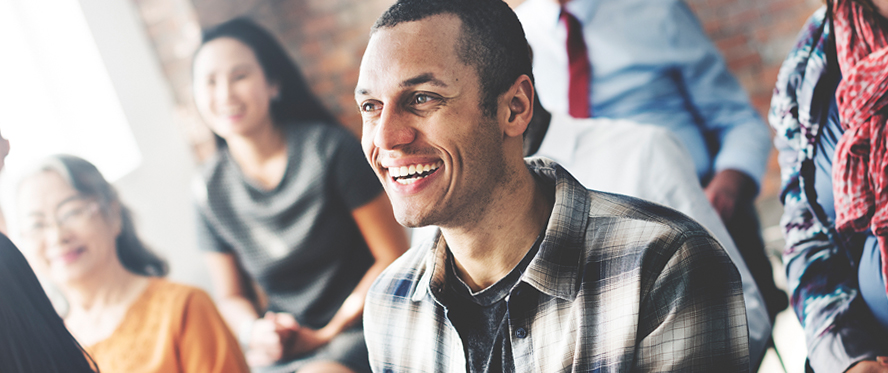 Man smiling in the foreground with other smiling people in the background.