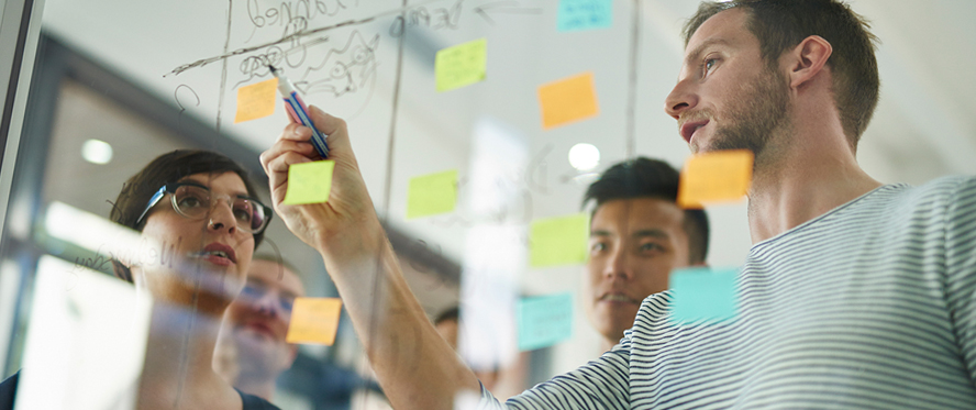 Man drawing a diagram on a window with Post-it notes attached to it.