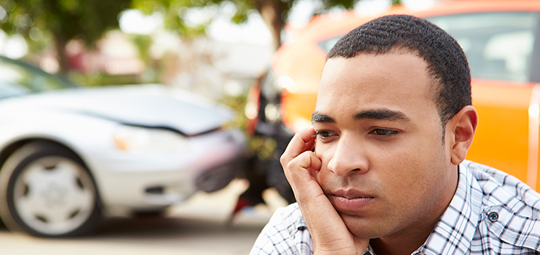 Man with hand on cheek looking pensive. The background shows a rear-end auto accident.