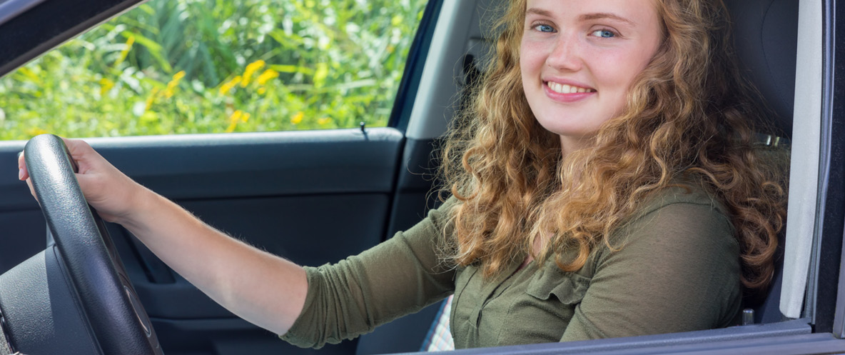 Woman in car with hand on steering wheel smiling