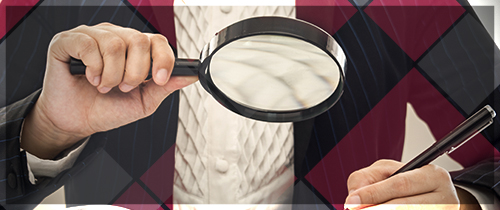 Someone holding a magnifying glass in one hand and a pen in the other hand looking over a document