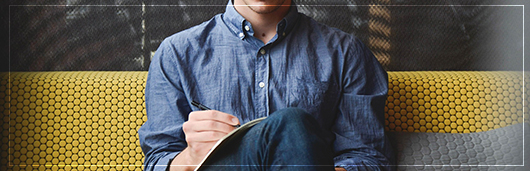 Man sitting on a couch with notebook and pen in hand