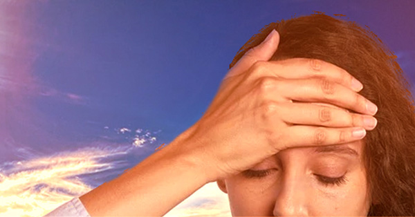 Woman with her hand over her forehead with the sun and blue sky in the background