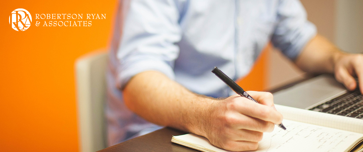 Man working at desk with pen and paper. Robertson Ryan logo, top left