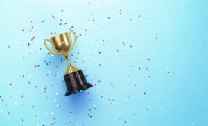 Colorful confetti falling over gold cup sitting over blue background. Horizontal composition with copy space. Directly above.