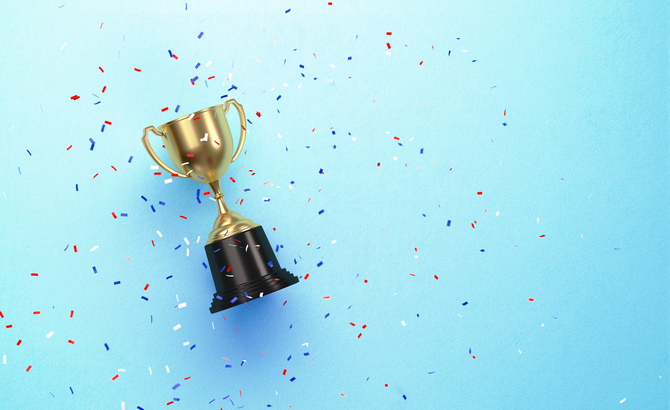 Colorful confetti falling over gold cup sitting over blue background. Horizontal composition with copy space. Directly above.